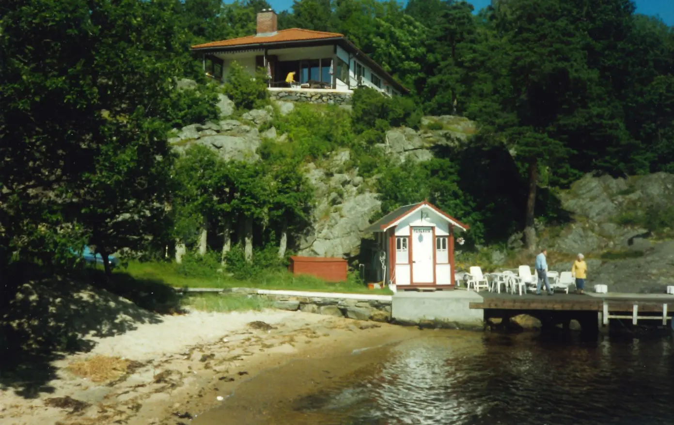 Børskiosken er hvitmalt, med røde detaljer, og står på en brygge ved en strand i Fugelviksund på Søm.