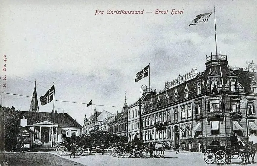 Børskioksen midten i Børsparken. I gata foran er det flere hestevogner, og det norske flagg er heist i tre flaggstenger. Til høyre kan man se Ernst hotel