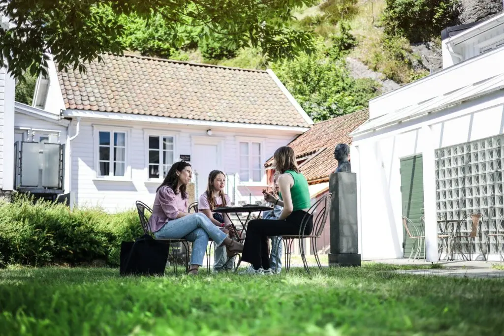 Bildet viser fire personer som sitter i hagen til Vigeland hus og drikker kaffe og spiser vafler.