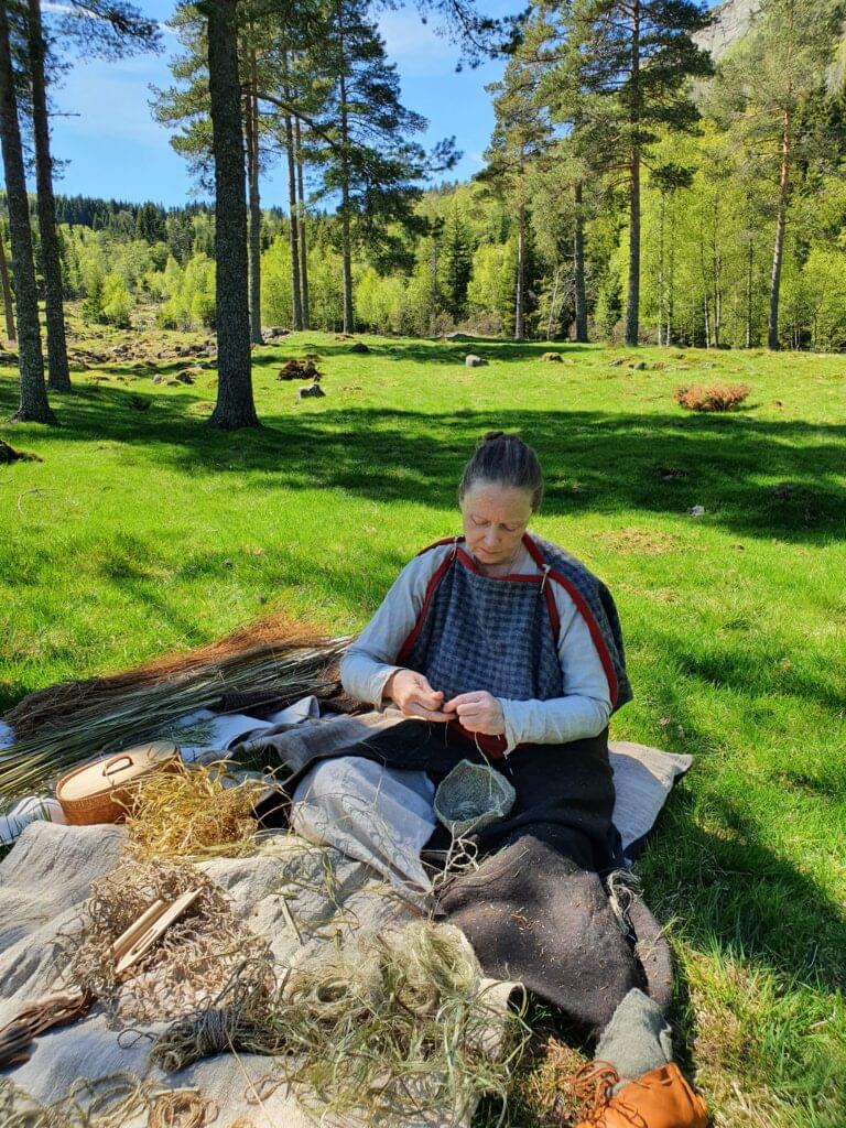 Kari sitter med ulike plantefibre på fangen på Sosteli jernaldergård. Hun har på seg tidsriktig antrekk av ull.