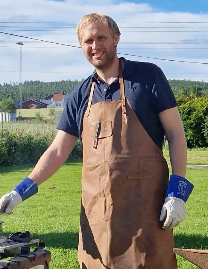 En høy, blond mann står smilende ved smie.